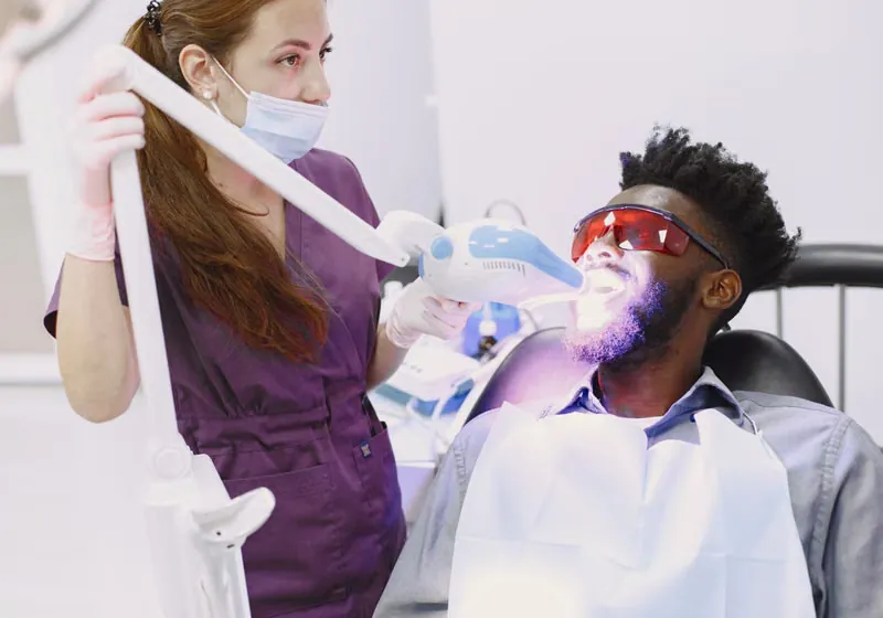 Dental professional applying UV curing light during professional teeth whitening at Deekshu Dental Sarjapura Bangalore