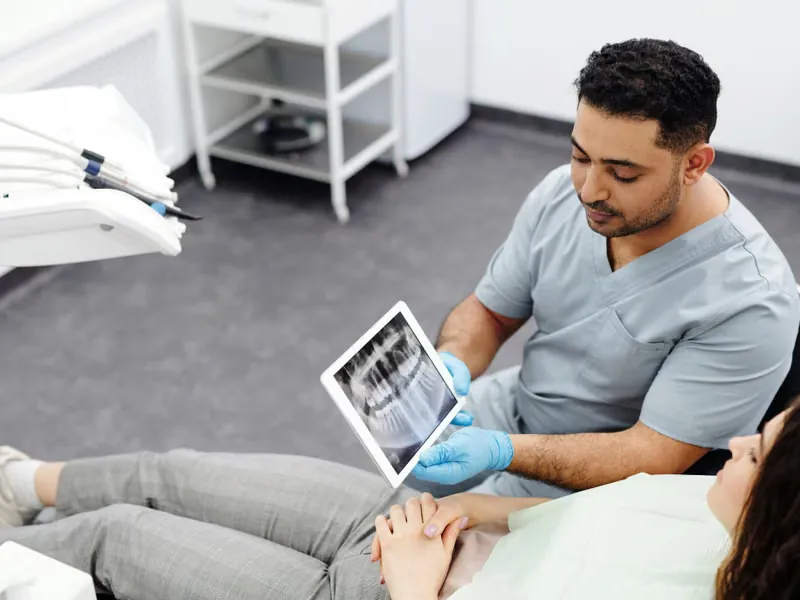 Dentist showing TMJ X-ray results on tablet to patient during jaw disorder consultation at Deekshu Dental Bangalore